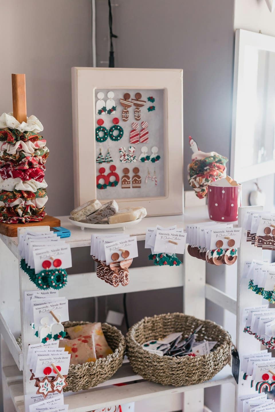 Handmade Christmas earrings and festive scrunchies displayed on wooden shelves.
