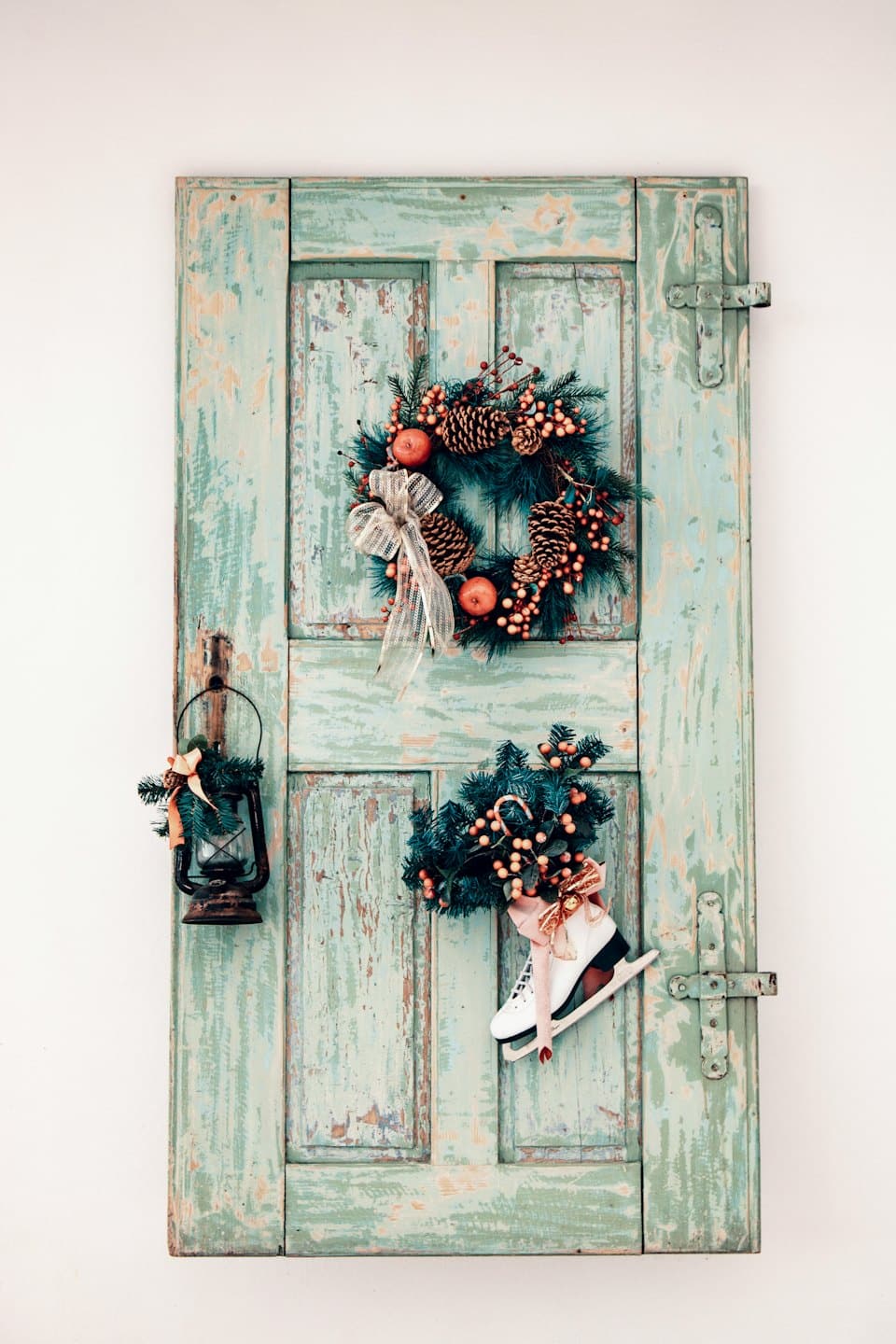 Holiday wreath and decorations hang on a weathered green door.