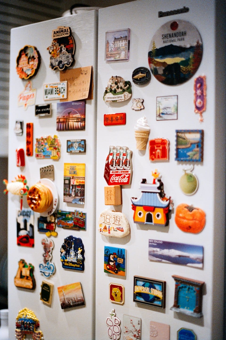 Refrigerator door covered with many colorful souvenir magnets and notes.